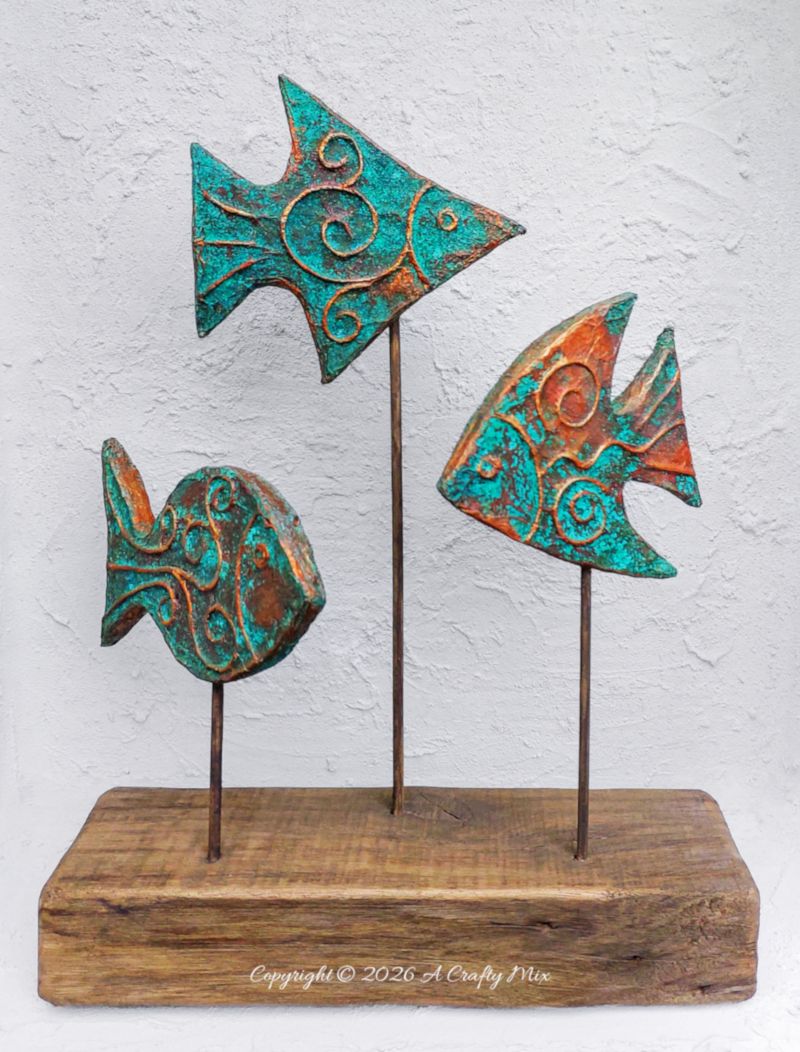 Three rustic patina fish on wooden sticks used as DIY coastal decor, crafted from layered cardboard and copper tape.