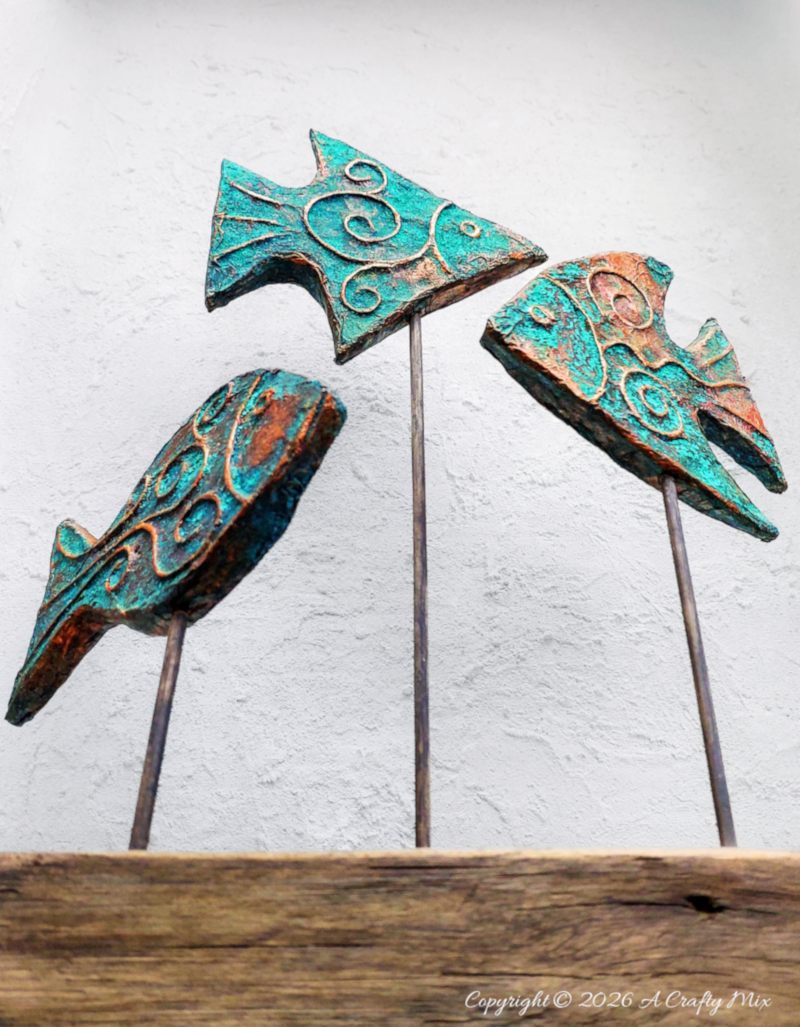 Three copper fish on skewers above a wooden block