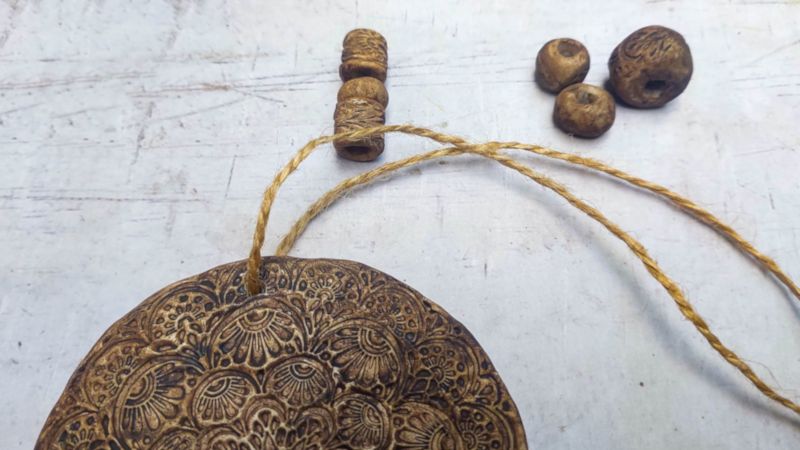 Thread twine through the holes in the boho clay medallion