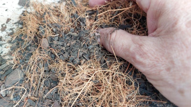 Hand mixing a chunky potting soil with loose strands of coconut coir, showing a textured, airy planting mix up close.