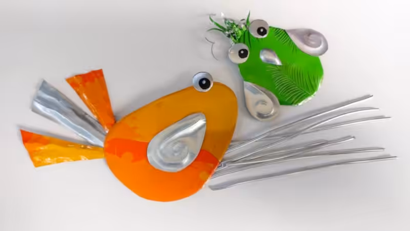 Partially assembled orange and green soda can birds lying flat next to several long pieces of silver wire for their legs.