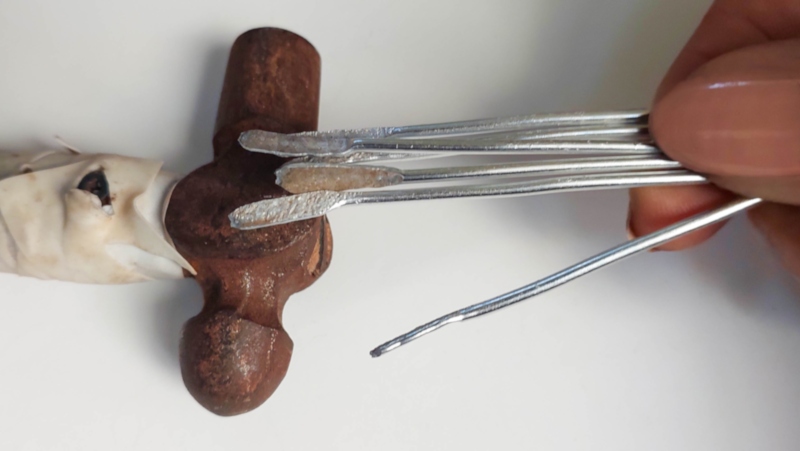 Close‑up of several pieces of silver jewellery wire with hammer‑flattened tips, showing how to create small feet for soda can bird legs.