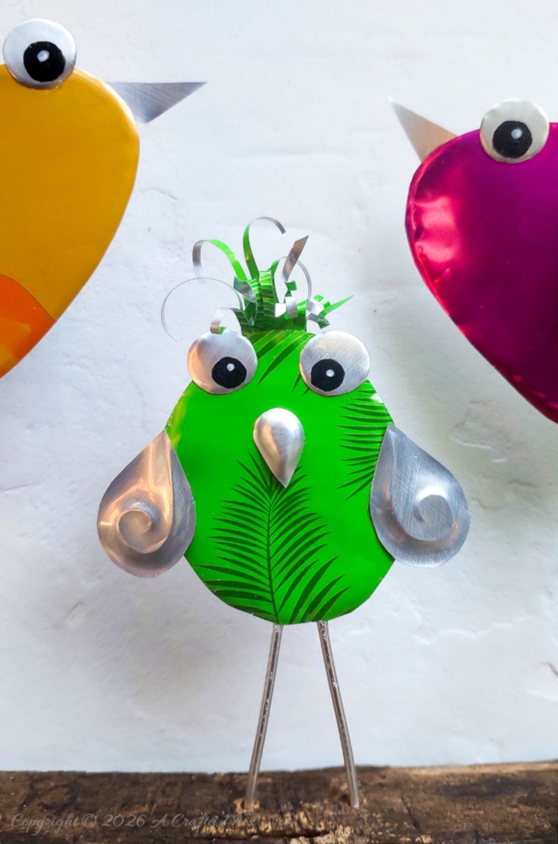 Close up of a bright green recycled Soda Can Bird made from an aluminium drink can with large eyes and embossed metal wings.