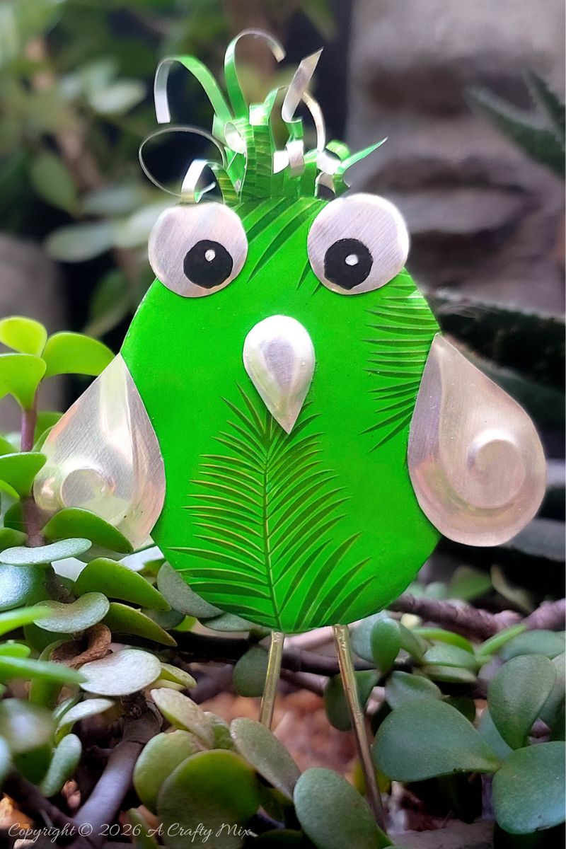 Close up of a bright green recycled Soda Can Bird made from an aluminium drink can with large eyes and embossed metal wings.