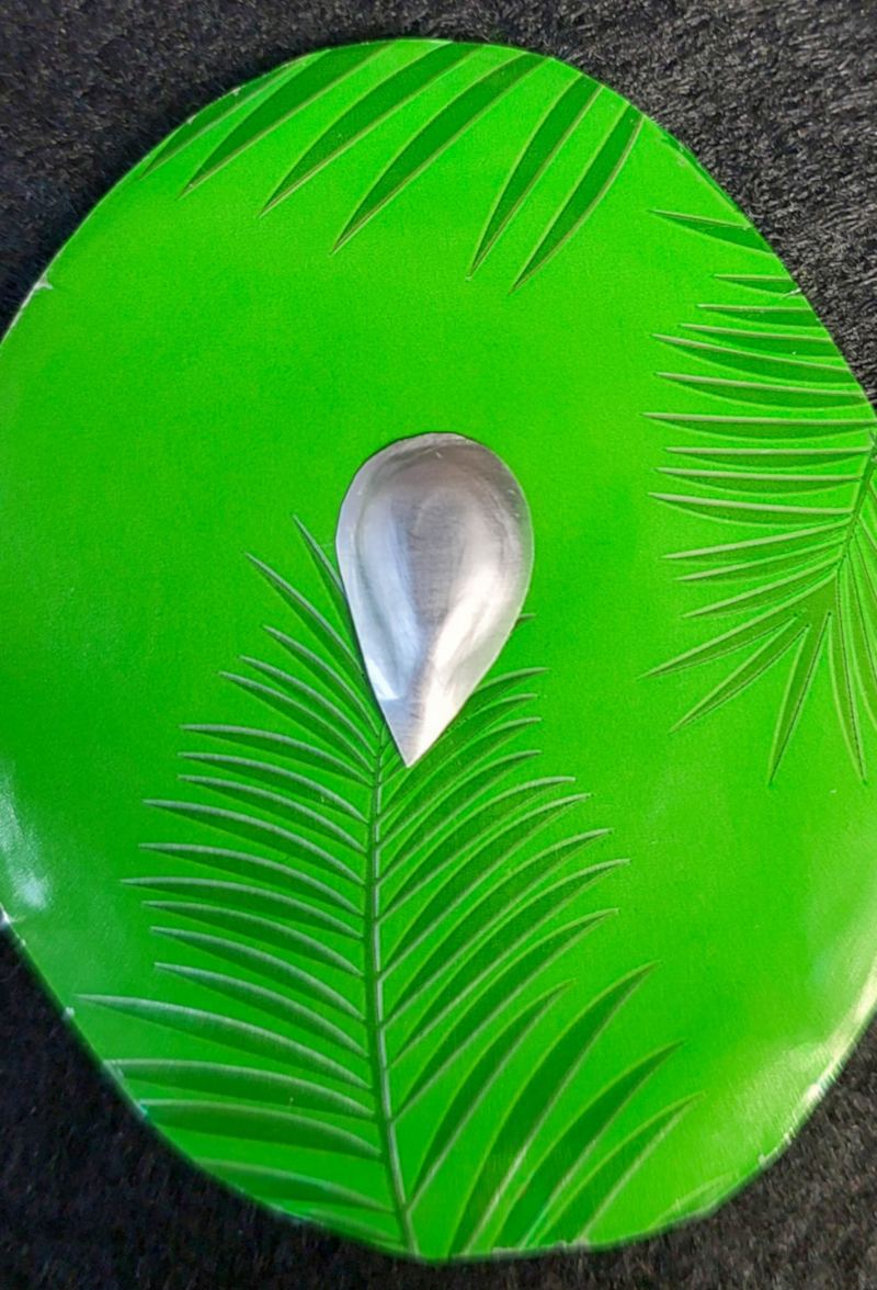 Close‑up of a raised silver teardrop beak embossed on a round green soda can bird body with leaf patterns.