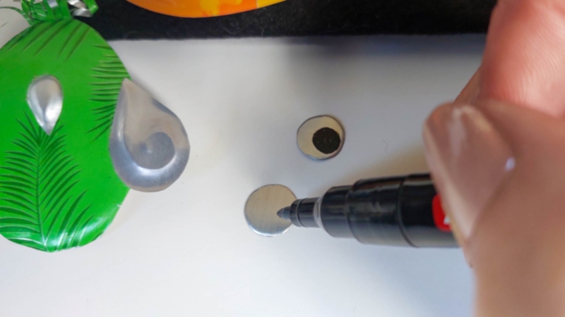 A hand drawing a dot on an aluminium circle with a black permanent marker.