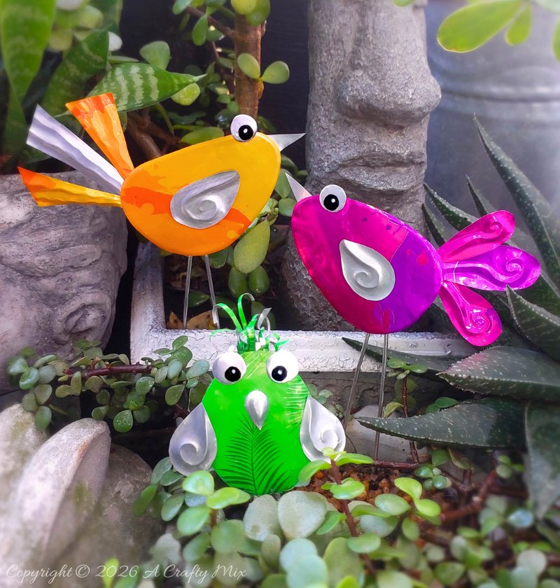 Orange, pink and green recycled Soda Can Birds on wire legs decorating potted plants in a small garden.