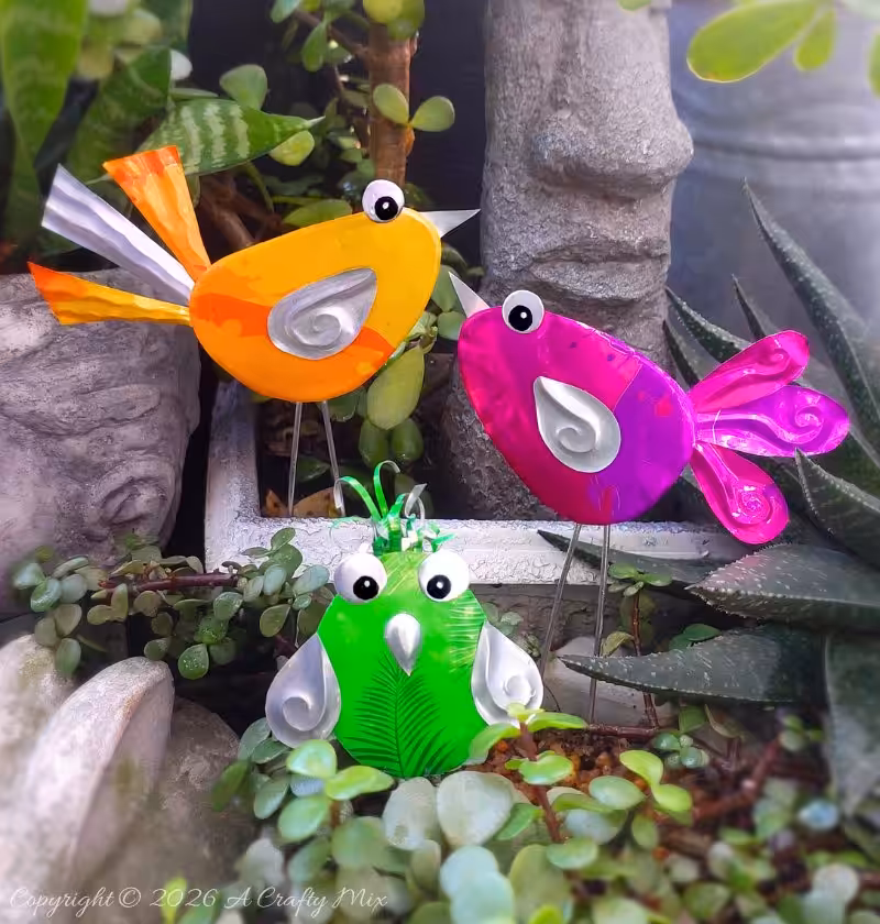 Orange, pink and green recycled Soda Can Birds on wire legs decorating potted plants in a small garden.
