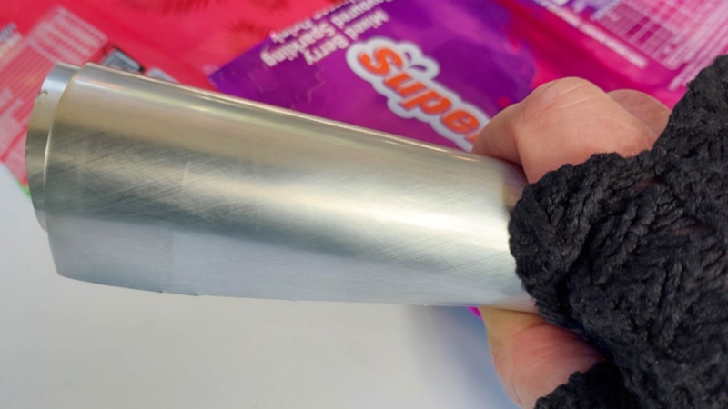 Hand wearing a dark glove rolling a cut aluminium soda can into a smooth curved sheet to flatten it for making recycled Soda Can Birds.