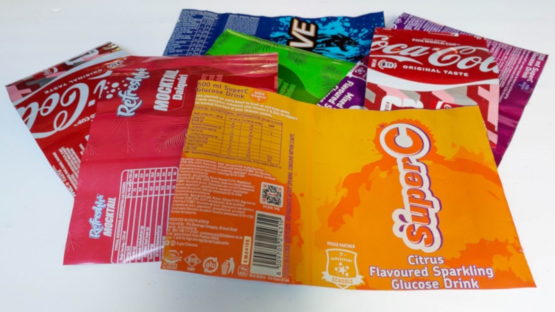 Several flattened, colourful soda cans cut into rectangular sheets and fanned out on a white surface, ready to be used for a recycled Soda Can Birds craft.