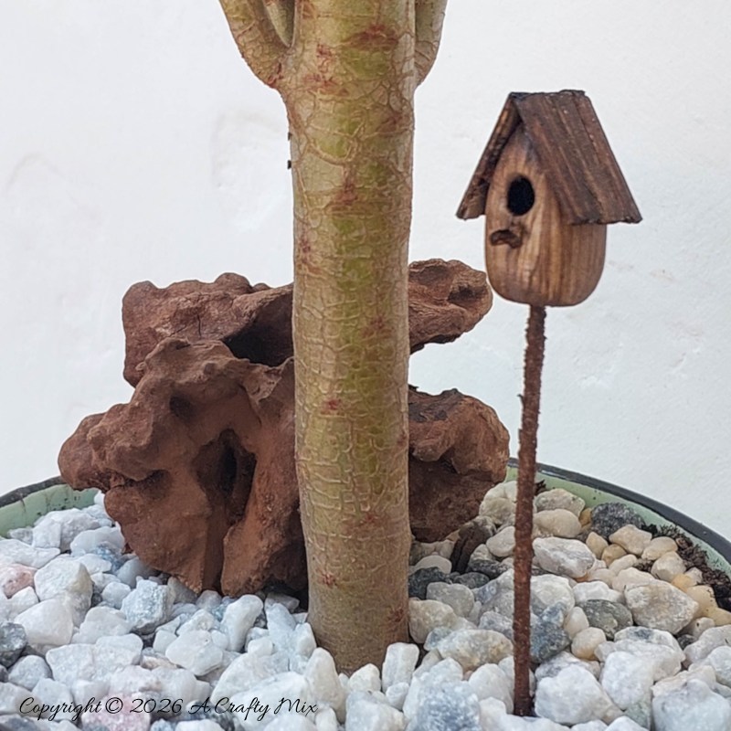 A close up of a miniature bird house in a mug garden