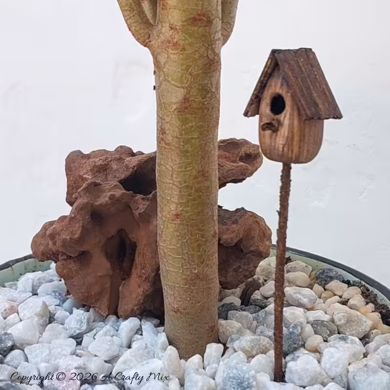A close up of a miniature bird house in a mug garden