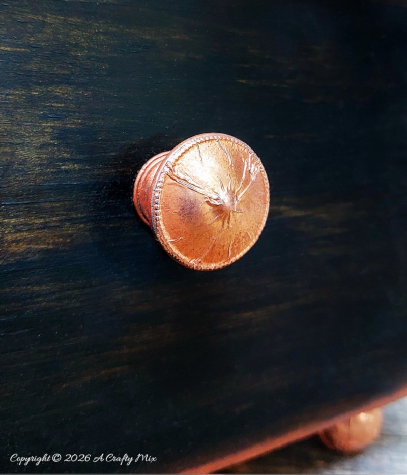 A close up of a small copper knob on a dark wooden background