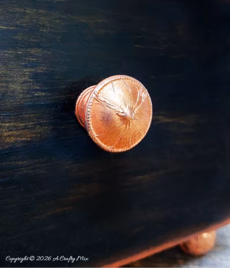 A close up of a small copper knob on a dark wooden background