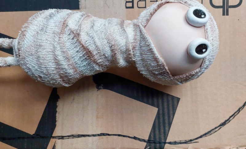 Make a tiny sarcophagus from scrap cardboard for your DIY Halloween mummy. This easy upcycling step shows how simple cardboard strips and a curved base become the shape for a weathered faux-stone tomb. Save it for your next not-too-spooky Halloween craft.