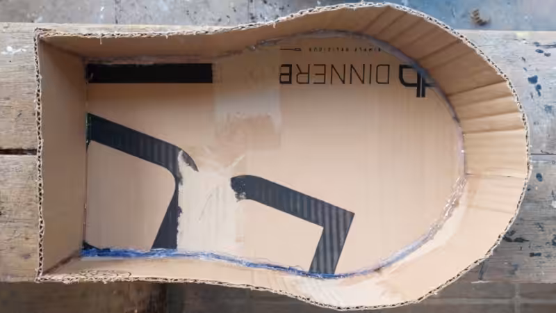 Two-step collage showing cardboard strips and a curved cardboard sarcophagus base being assembled with hot glue on a wooden work surface.