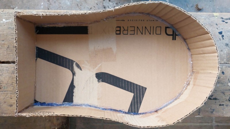 Two-step collage showing cardboard strips and a curved cardboard sarcophagus base being assembled with hot glue on a wooden work surface.