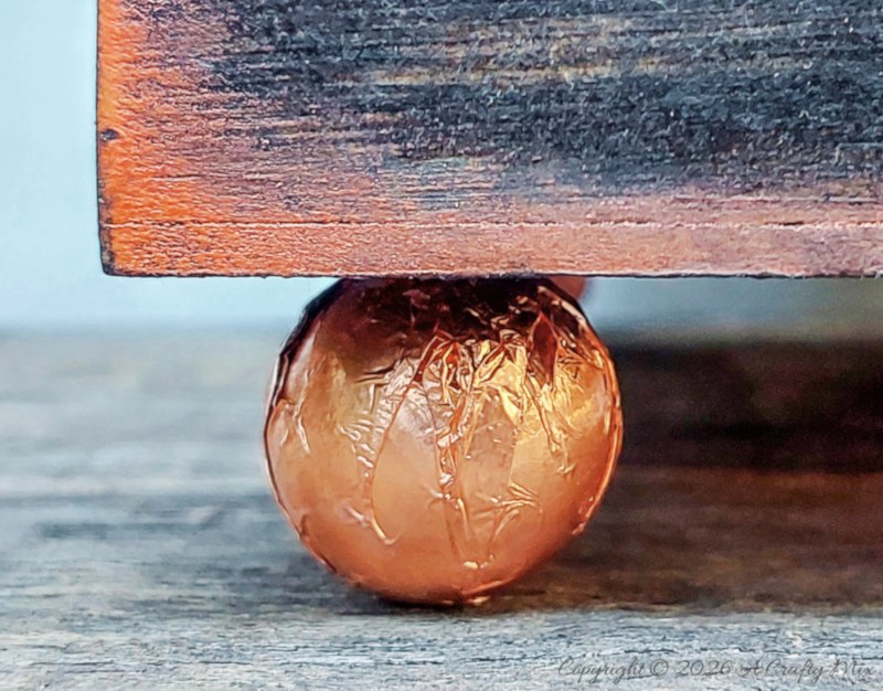 Close-up of a round copper-covered bead used as a decorative foot under the corner of a wooden planter.