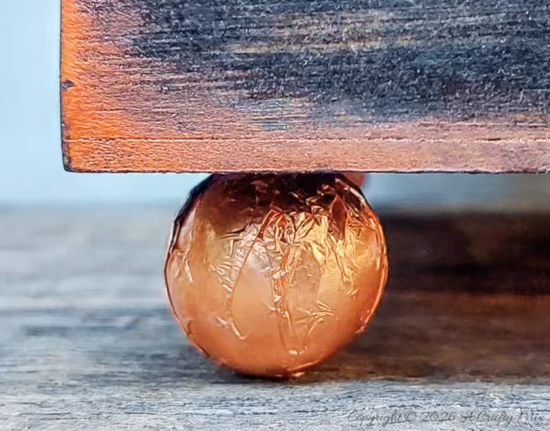 Close-up of a round copper-covered bead used as a decorative foot under the corner of a wooden planter.