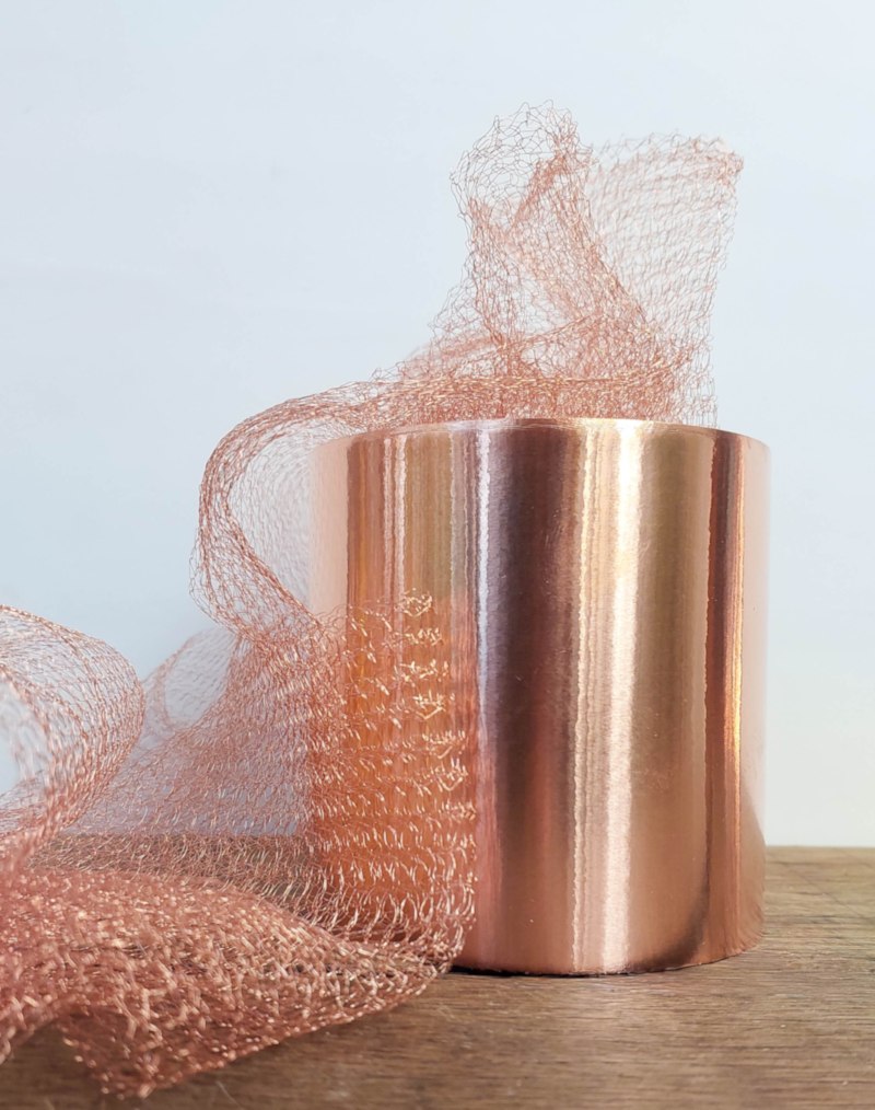 Shiny roll of copper tape with loose copper mesh that help keep snails away, displayed on a wooden surface against a light background.