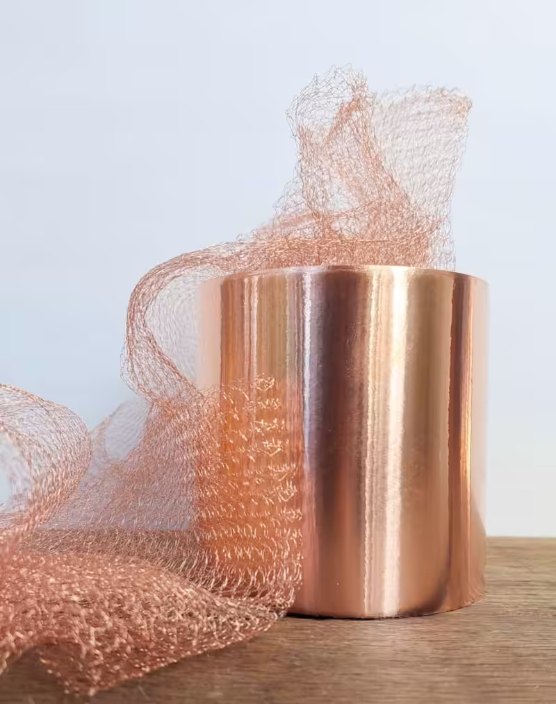 Shiny roll of copper tape with loose copper mesh that help keep snails away, displayed on a wooden surface against a light background.
