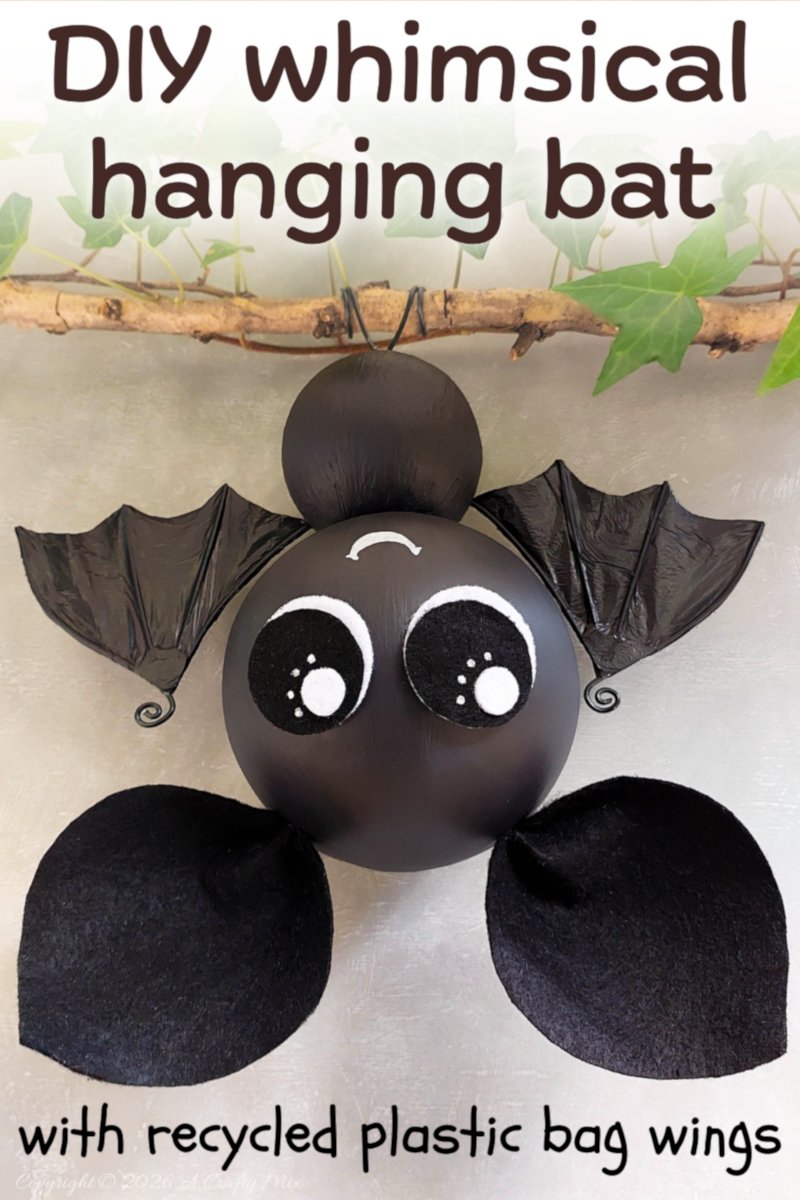 Pin graphic of a cute black hanging bat with large eyes, recycled plastic bag bat wings, and black wire feet, hanging from an ivy-covered branch.