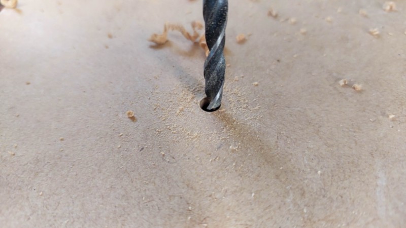 A drill bit drilling into the bottom of a wooden planter