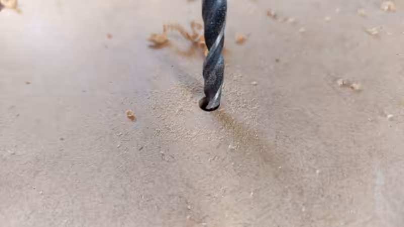 A drill bit drilling into the bottom of a wooden planter
