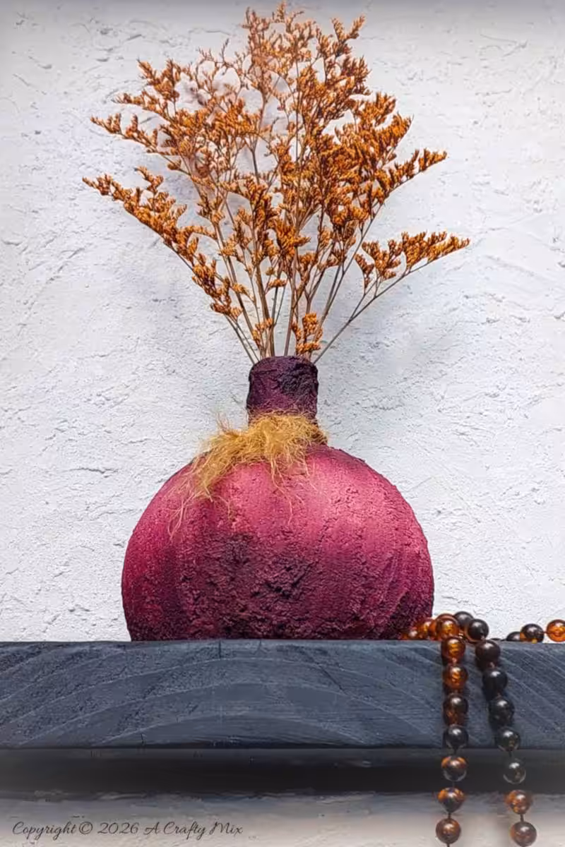 Upcycled faux ceramic Plum Noir vase with rough texture and jute tassel, styled with amber bead strands on a dark surface.