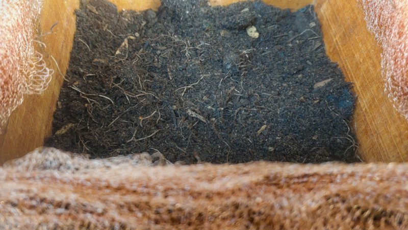 A rich soil mixture at the bottom of a wooden planter