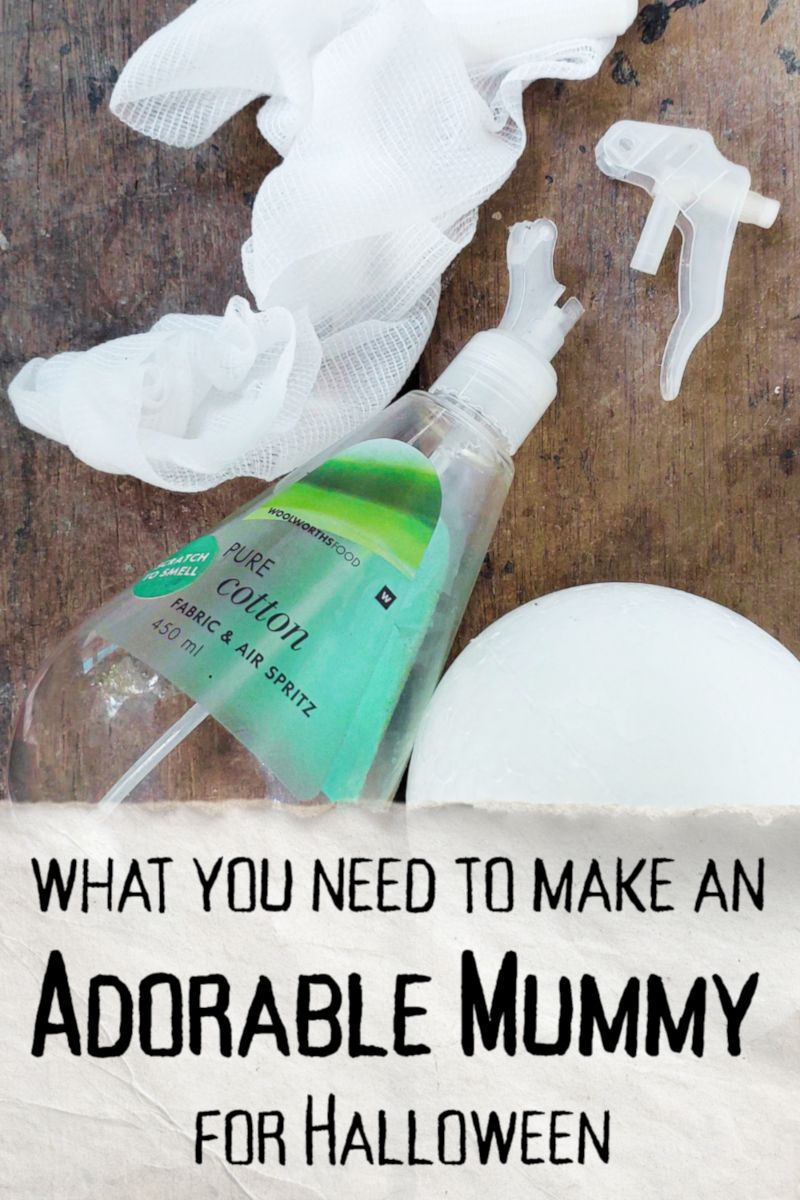 DIY Halloween mummy supply photo showing white gauze, a clear plastic bottle with green label, detached spray top, and a white foam ball on a rustic wooden surface.