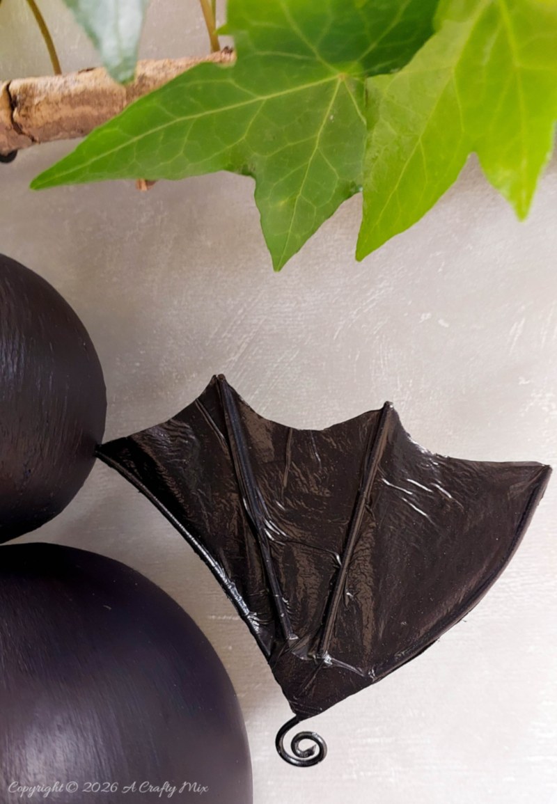 Close-up of one shiny black recycled plastic bag bat wing with raised vein details and a curled wire tip.