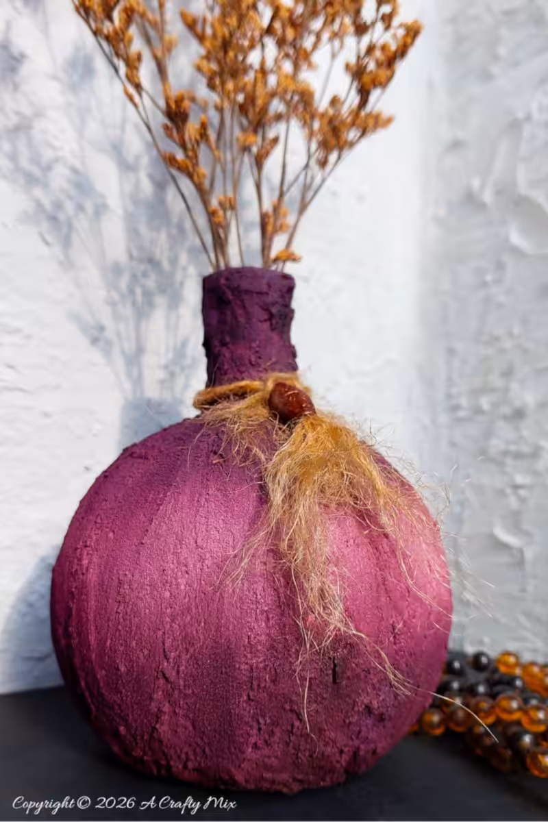 Tall dried stems arranged in a deep, textured DIY plum vase, displayed against a white plaster wall for moody boho décor