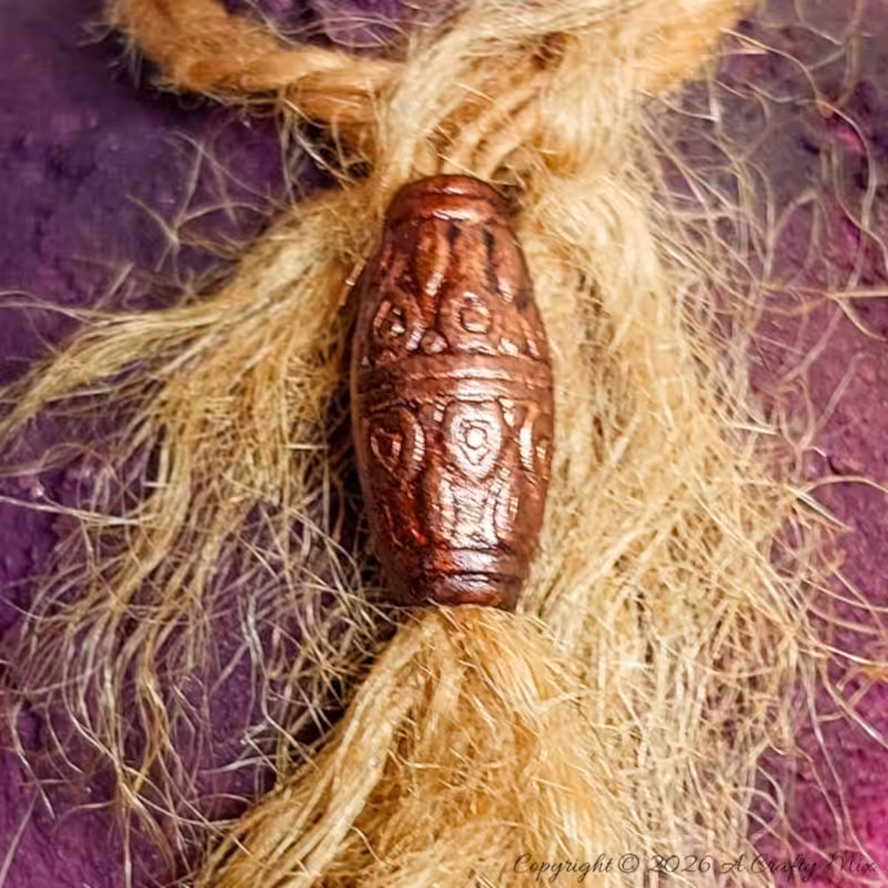 Close-up of a carved copper-toned bead tied onto rough jute twine, wrapped around the neck of a textured Plum Noir DIY vase
