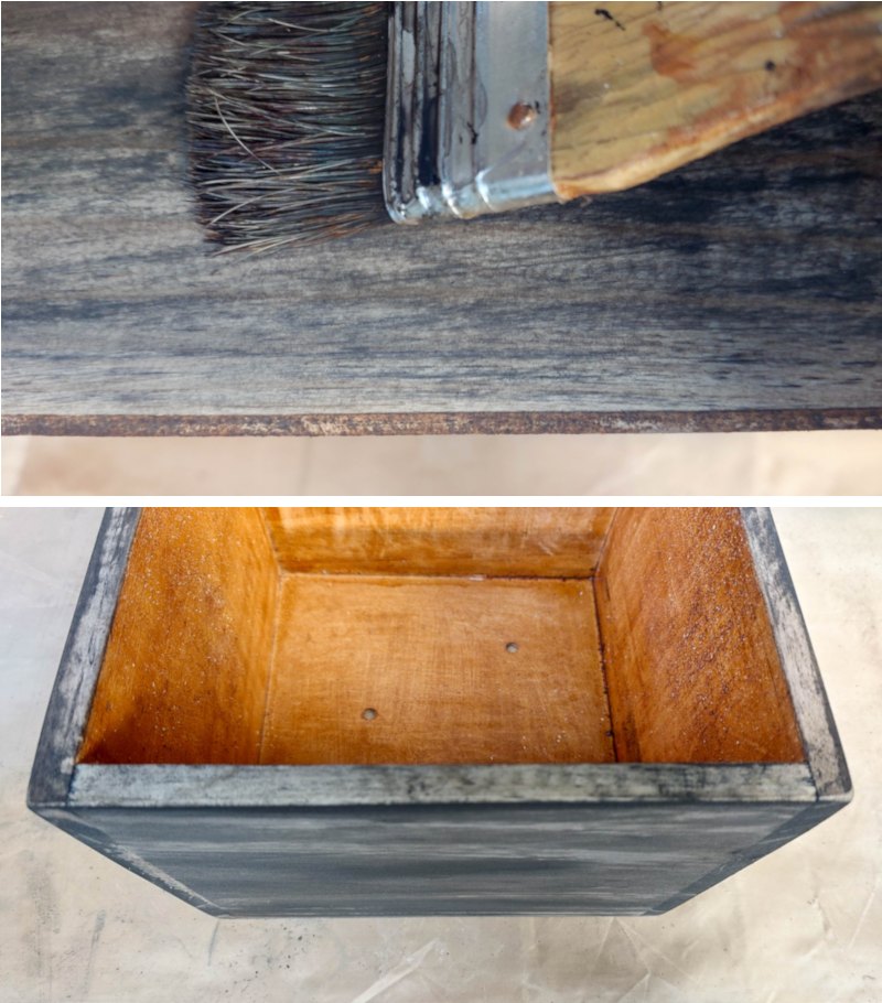 A paint brush applying watered down black paint to the outside of a wooden box.