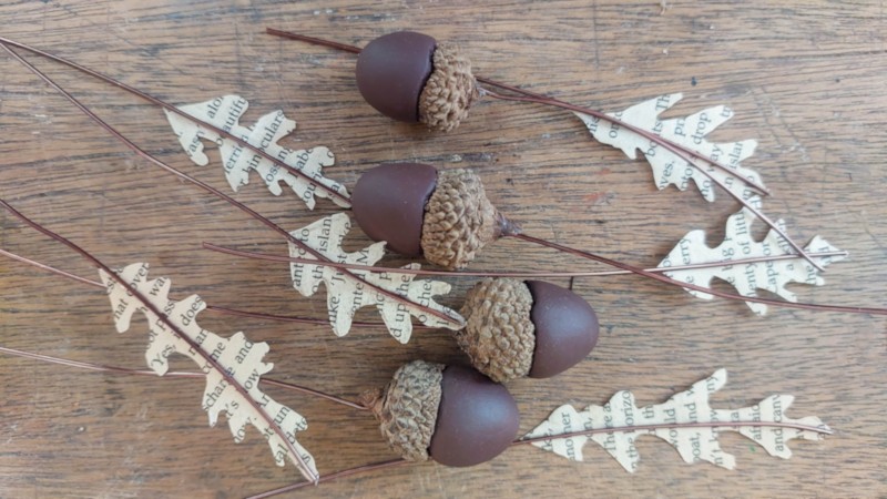 Book page leaves with wire stems and clay acorns on a wooden background