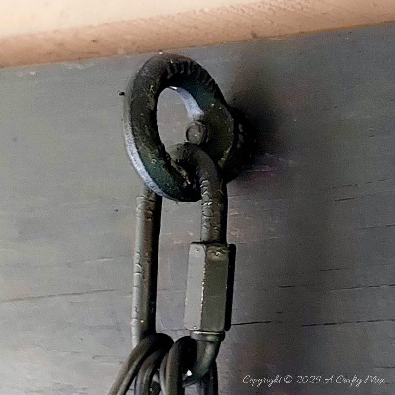 A close up of a eye bolt and carabiner on a wooden beam