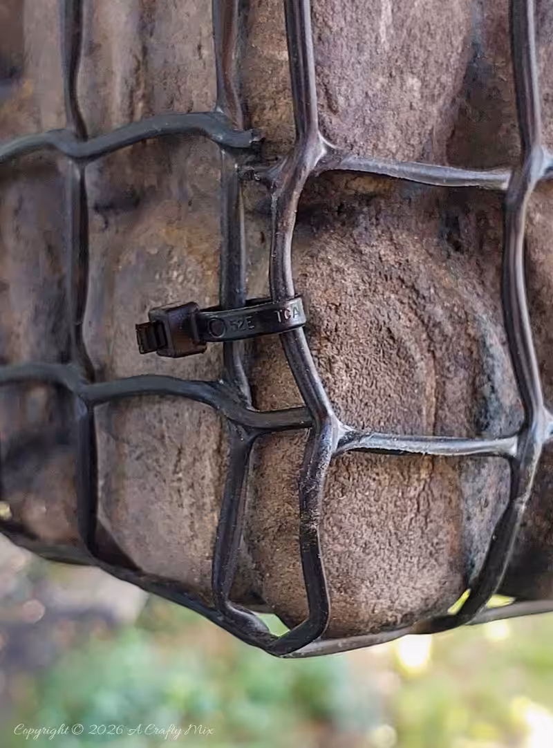 Close-up of black wire mesh wrapped around painted faux pebbles on a lightweight gabion planter