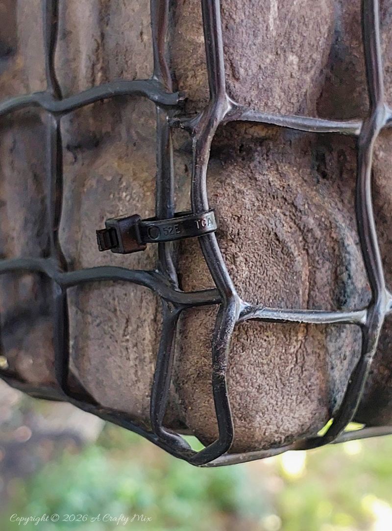 Close-up of black wire mesh wrapped around painted faux pebbles on a lightweight gabion planter