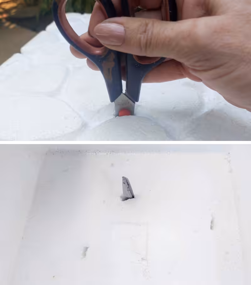 A hand poking holes into an EPS foam cooler with scissors