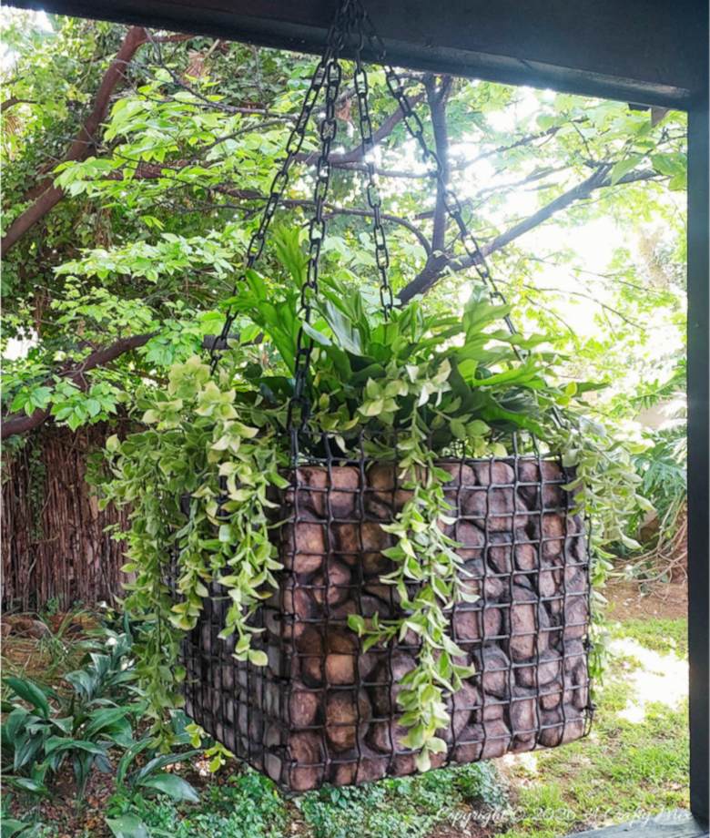 Side view of a lightweight hanging gabion planter filled with trailing greenery and faux rocks