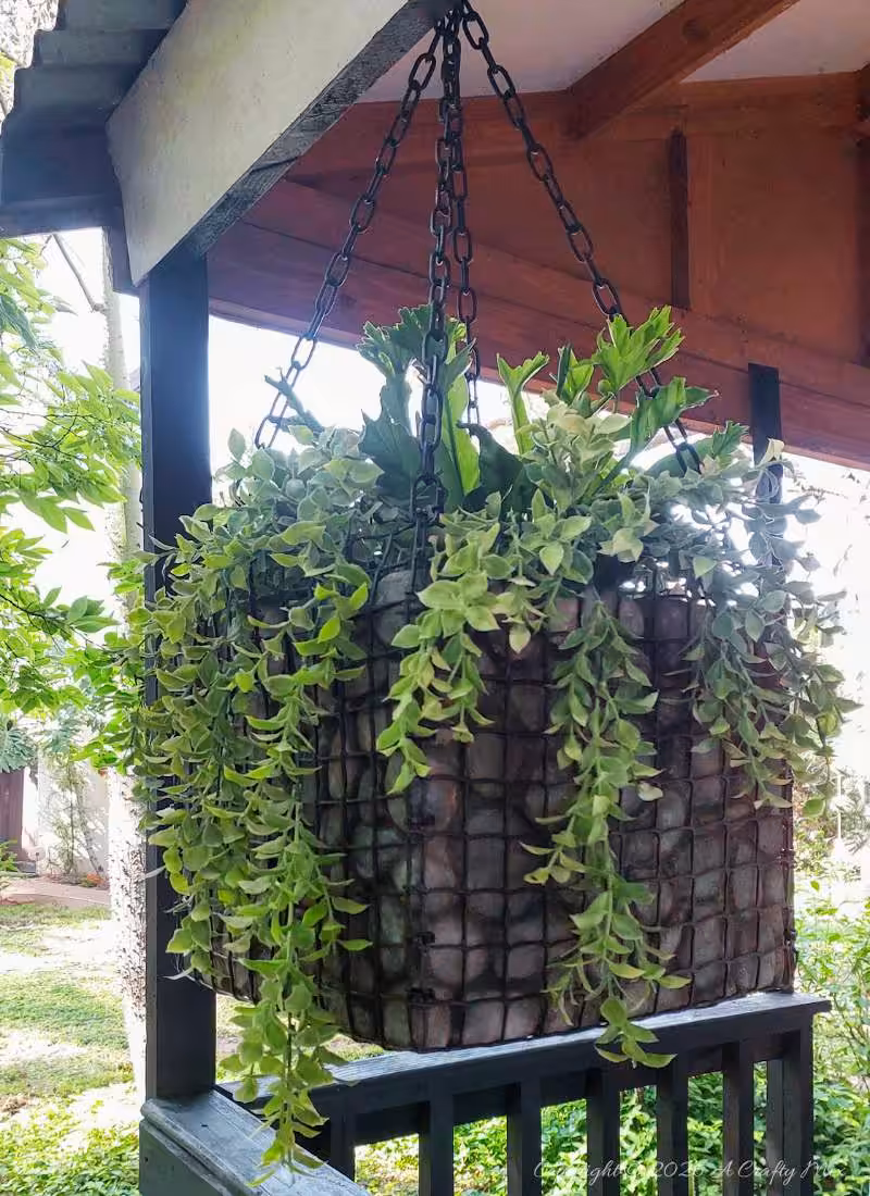 Finished hanging gabion planter with faux rocks and trailing plants suspended from black chains