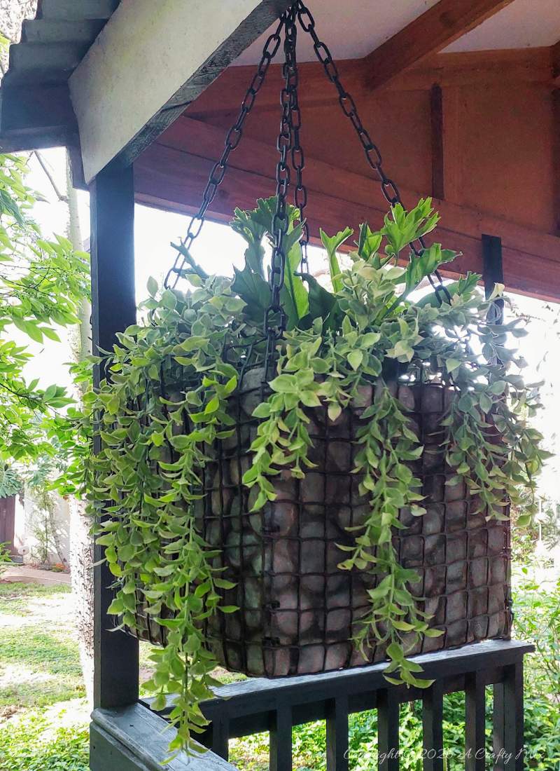 Finished hanging gabion planter with faux rocks and trailing plants suspended from black chains
