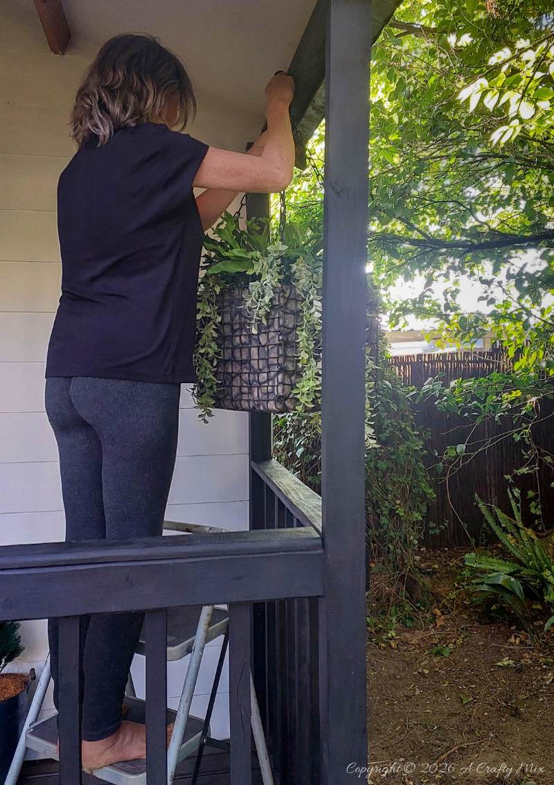 Woman standing on a step ladder while hanging a lightweight gabion planter from a patio beam