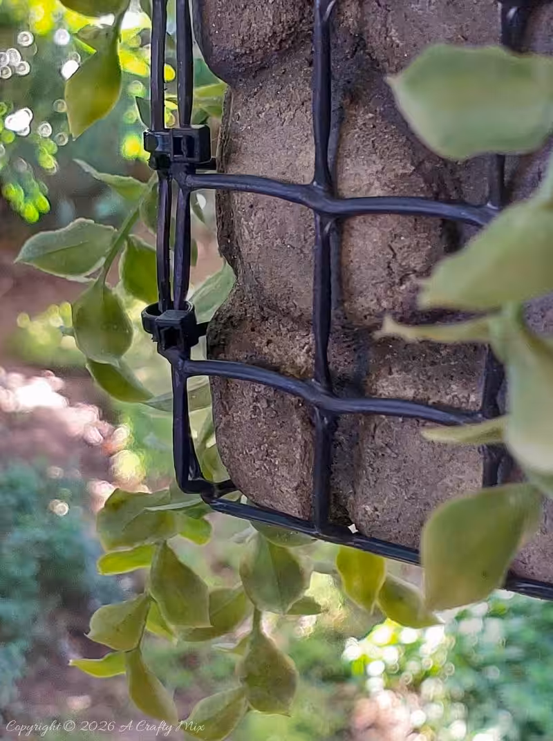 Close-up of realistic painted faux rocks behind black wire mesh on a DIY gabion planter