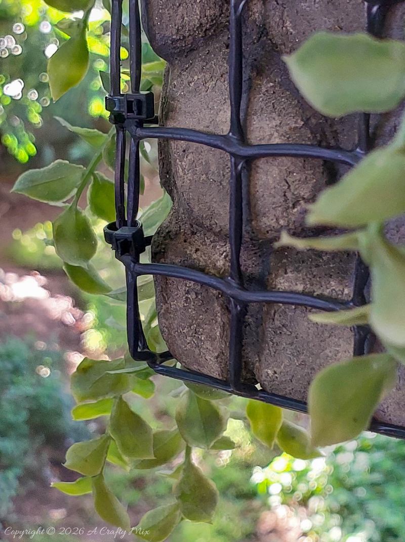 Close-up of realistic painted faux rocks behind black wire mesh on a DIY gabion planter