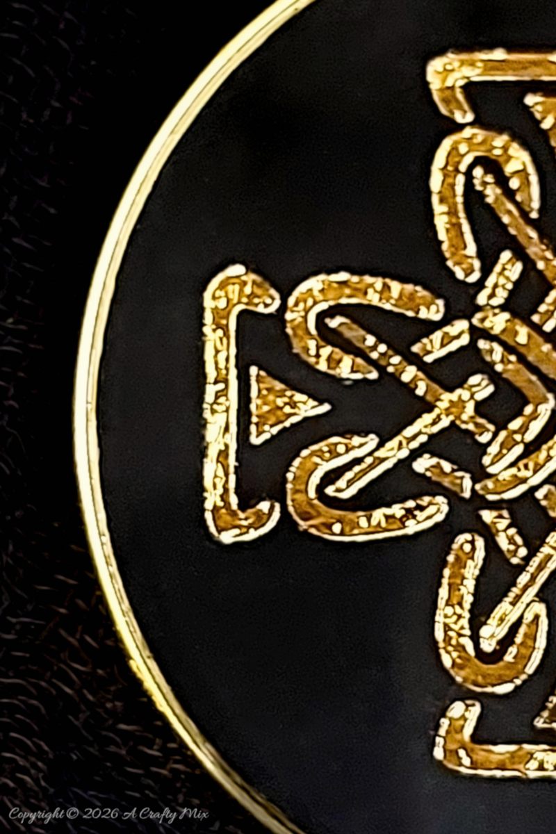Close-up of a gold Celtic knot design set in clear resin on a black background with a gold metal rim.