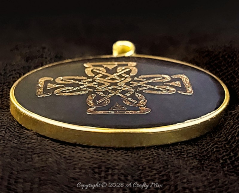 Side view of a handmade resin pendant showing a textured gold wire edge around clear resin.