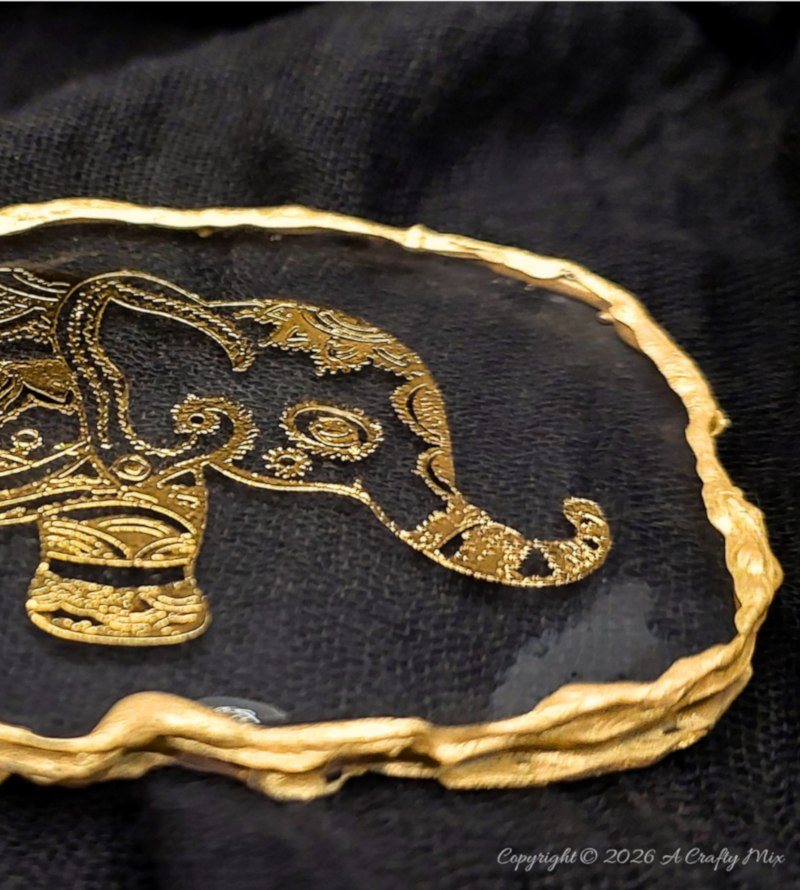 Close-up of a gold elephant design inside a clear resin keepsake with a textured gold edge.