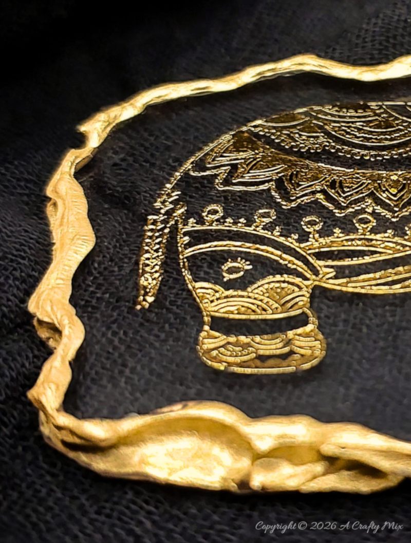 Close-up of the gold elephant head and trunk inside a glossy clear resin keepsake with a gold edge
